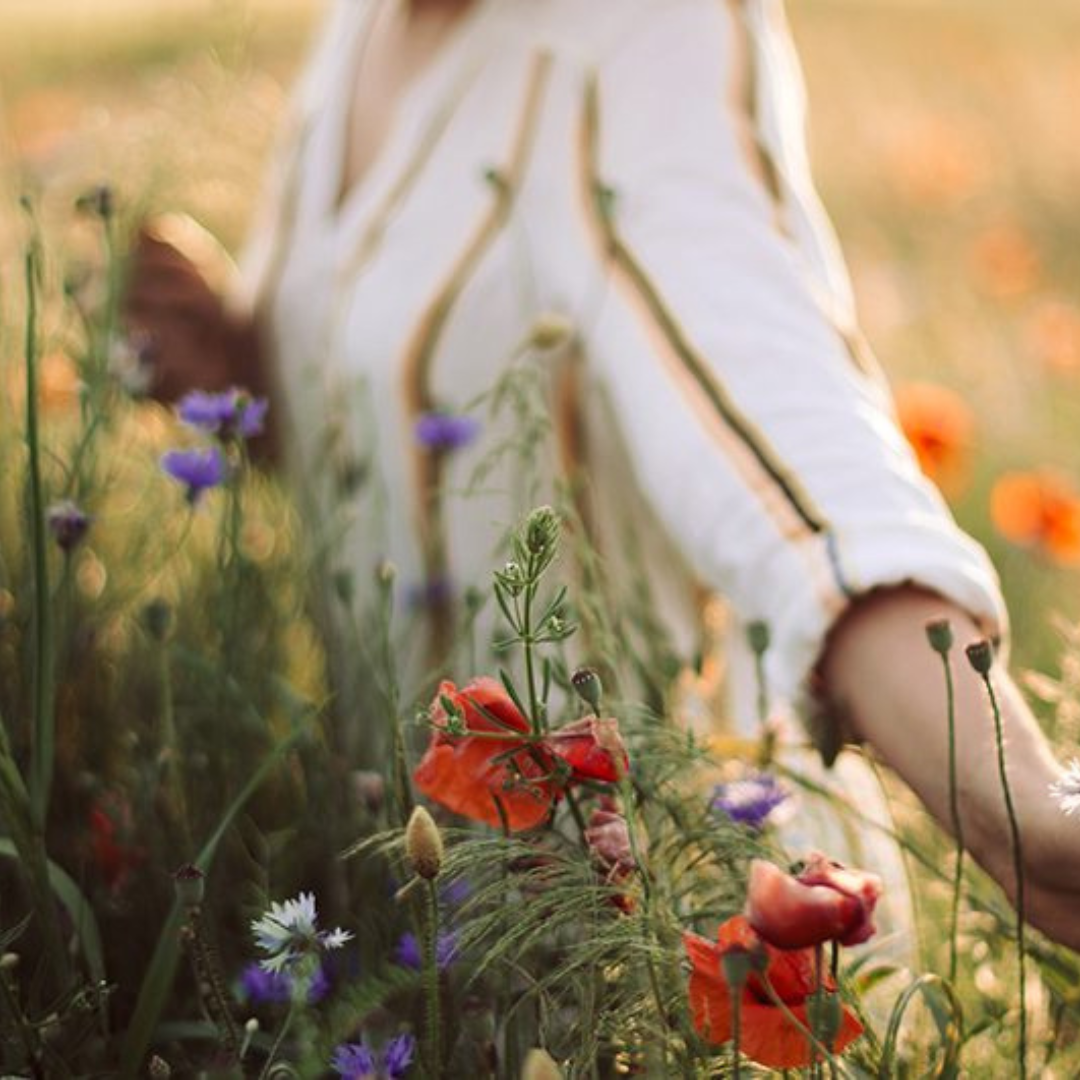 Osoba w białej koszuli przechadza się przez pole pełne kolorowych kwiatów.