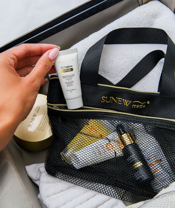 Osoba trzyma tubkę kremu przeciwsłonecznego SPF 50 obok kosmetyczki Sunew med+ z kosmetykami.